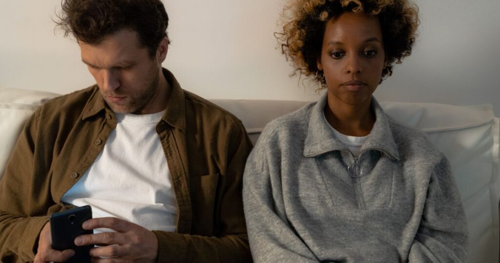 Pareja sentada en el sofá, distante, él mirando el móvil