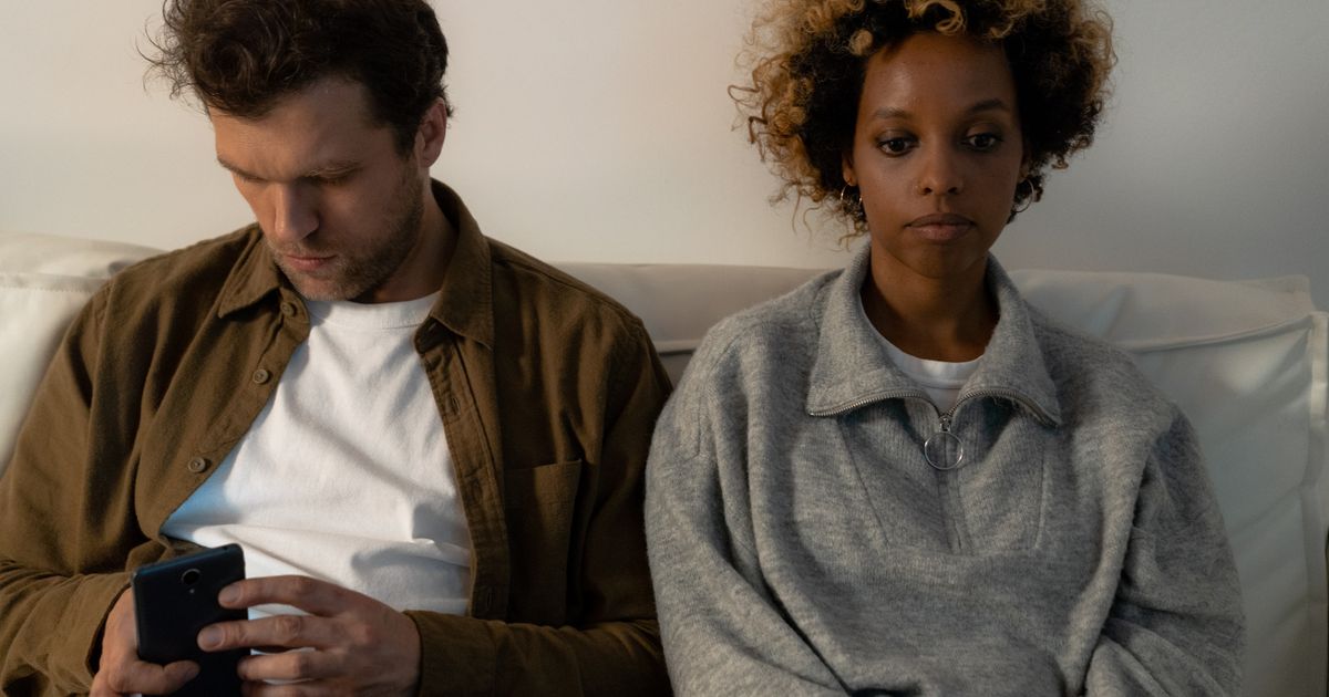 Pareja sentada en el sofá, distante, él mirando el móvil