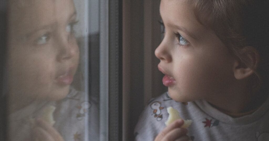 Niña mirando por la ventana con su reflejo en el cristal: EMDR en niños y adolescentes