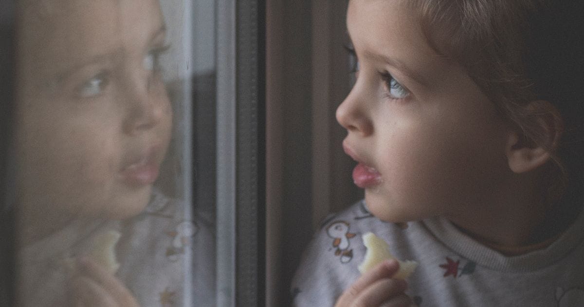 Niña mirando por la ventana con su reflejo en el cristal: EMDR en niños y adolescentes